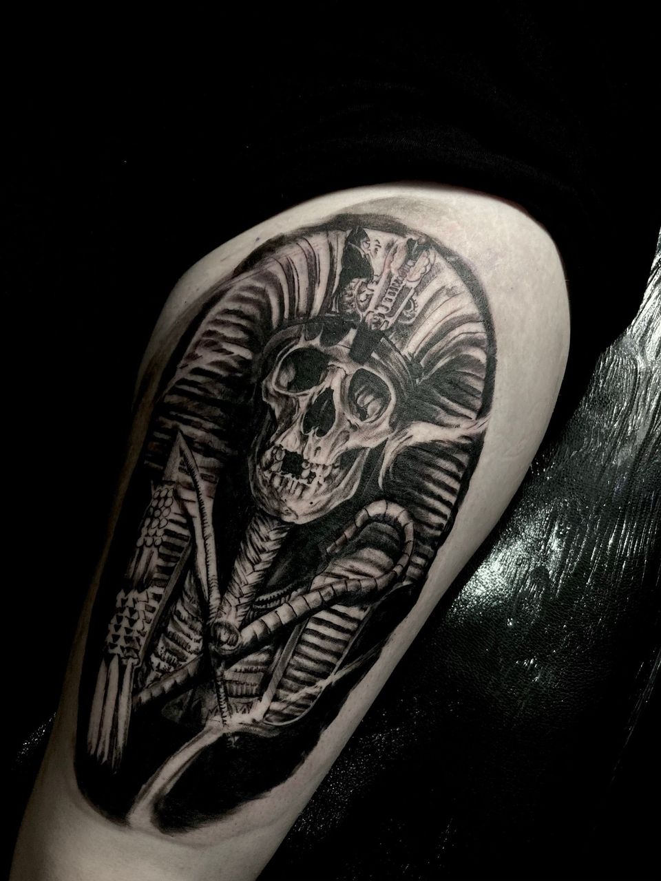 Black tattoo of a skull wearing a crown, wrapped in a cocoon-like design, on a person's arm.