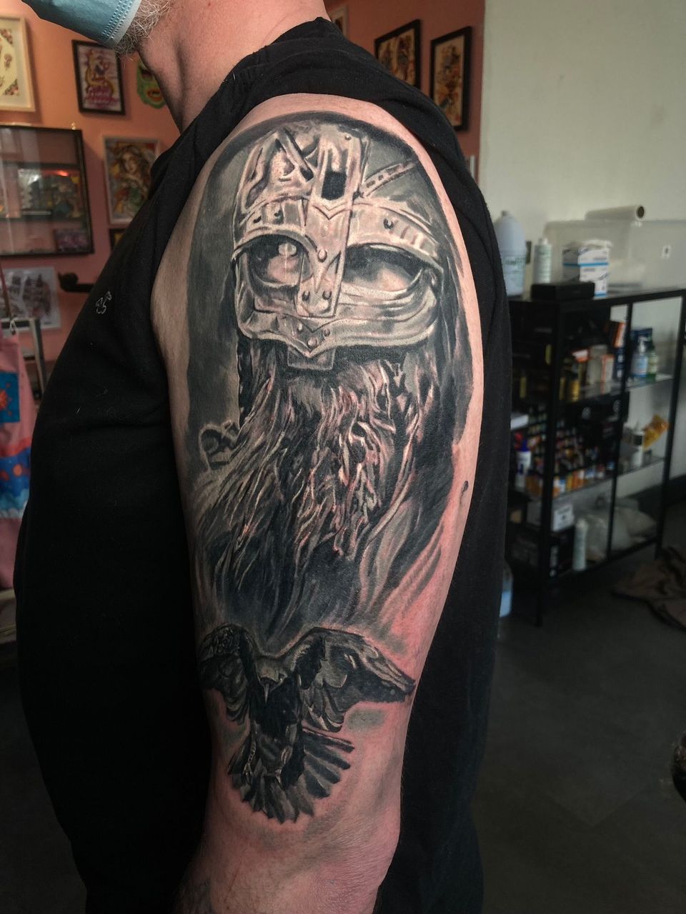 Tattoo of a Viking with a horned helmet and raven on a man's arm, in a tattoo parlor.