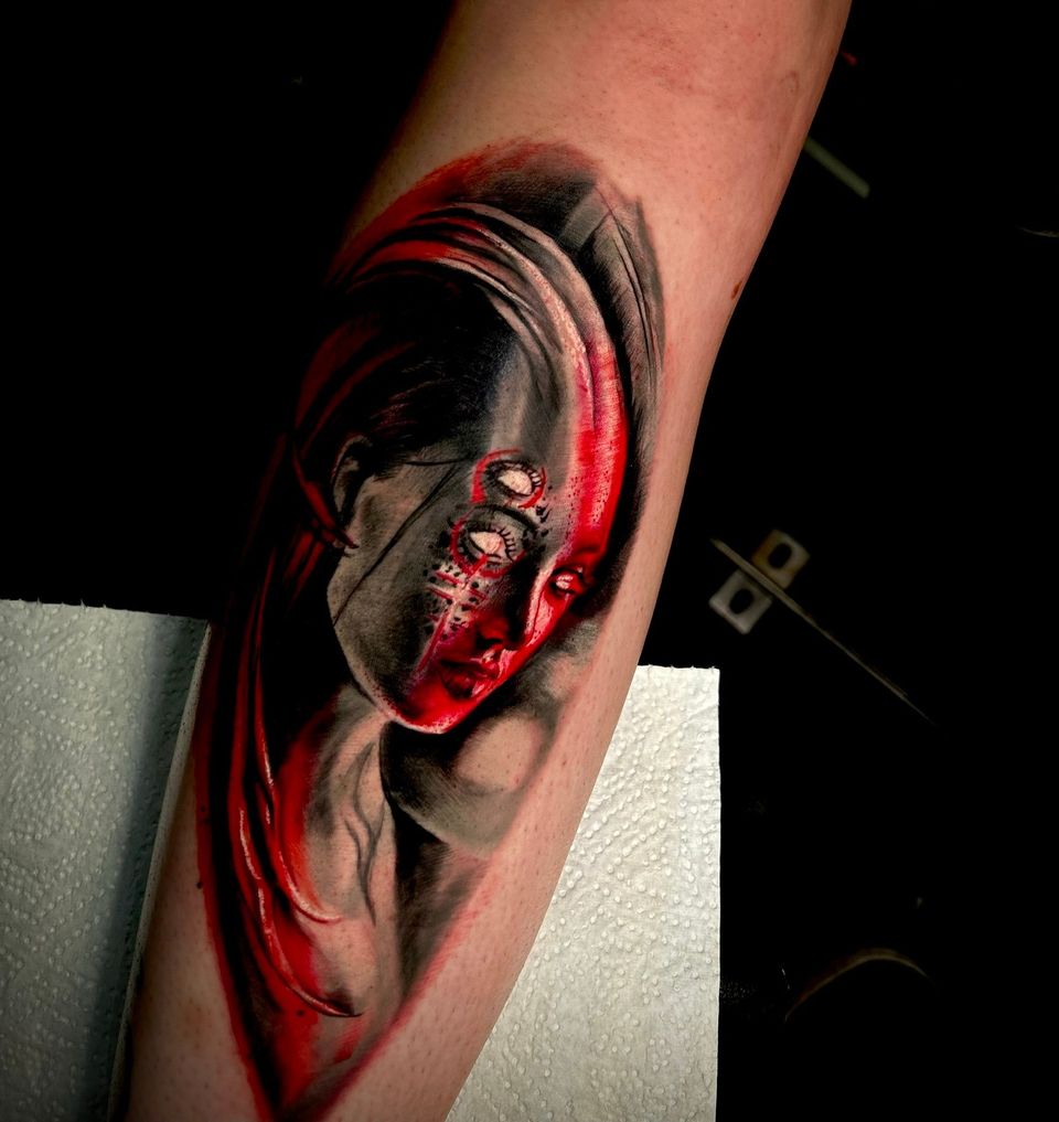 Tattoo of a person's face split with gray and red. The gray side is shadowed, while the red side has multiple eyes.