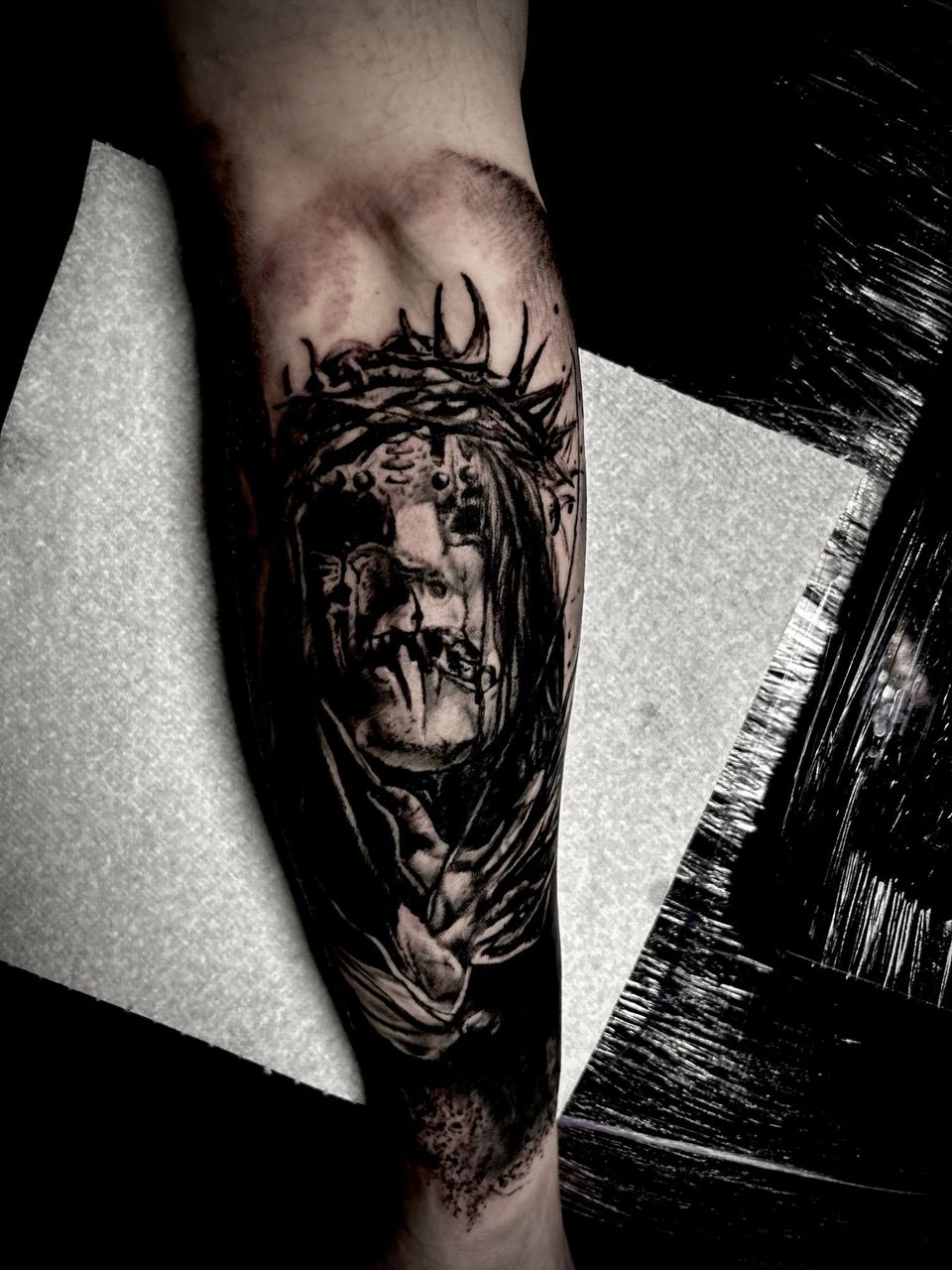 Tattoo of a figure with a crown of thorns, dark, detailed, on an arm.