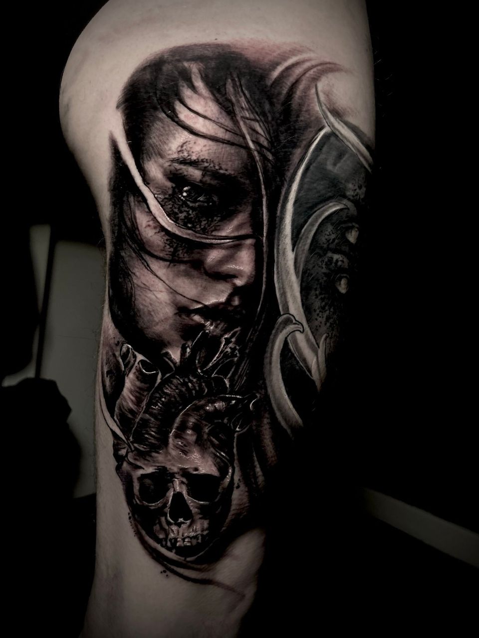 Detailed black and white tattoo on a leg. Features a woman's face, a skull, and decorative elements.